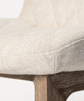 Close-up of a chair with a textured beige cushion and wooden legs on a white background