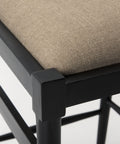 Close-up of a chair with a black frame and beige cushioned seat on a white background