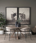 Dining room with a round wooden table and chairs, framed black and white pictures of cows on the wall, and a plant.