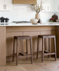 Two wooden bar stools in a modern kitchen with light wood cabinets and white countertops.