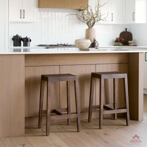 Two wooden bar stools in a modern kitchen with light wood cabinets and white countertops.