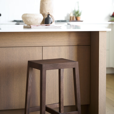 Wooden bar stool in front of a kitchen counter with a marble top.