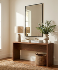 Wooden console table with decor items in a room with a large mirror and window.