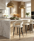 Modern kitchen with marble island, white stools, and gold pendant lights.