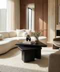 Modern living room with a beige sectional sofa, black coffee table, and decorative items.