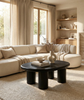 Modern living room with beige sectional sofa, black coffee table, and large windows.