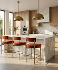 Modern kitchen with marble island, gold pendant lights, and orange stools.
