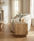 Modern living room with a white sofa, wooden side table, and decorative items.
