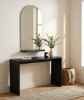 Black console table with mirror and decorative items in a room with a window and rug.