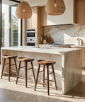 Modern kitchen with marble island, wooden stools, and stainless steel appliances.