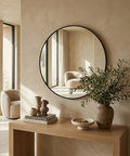 Round mirror on a beige wall above a wooden console table with decorative items.